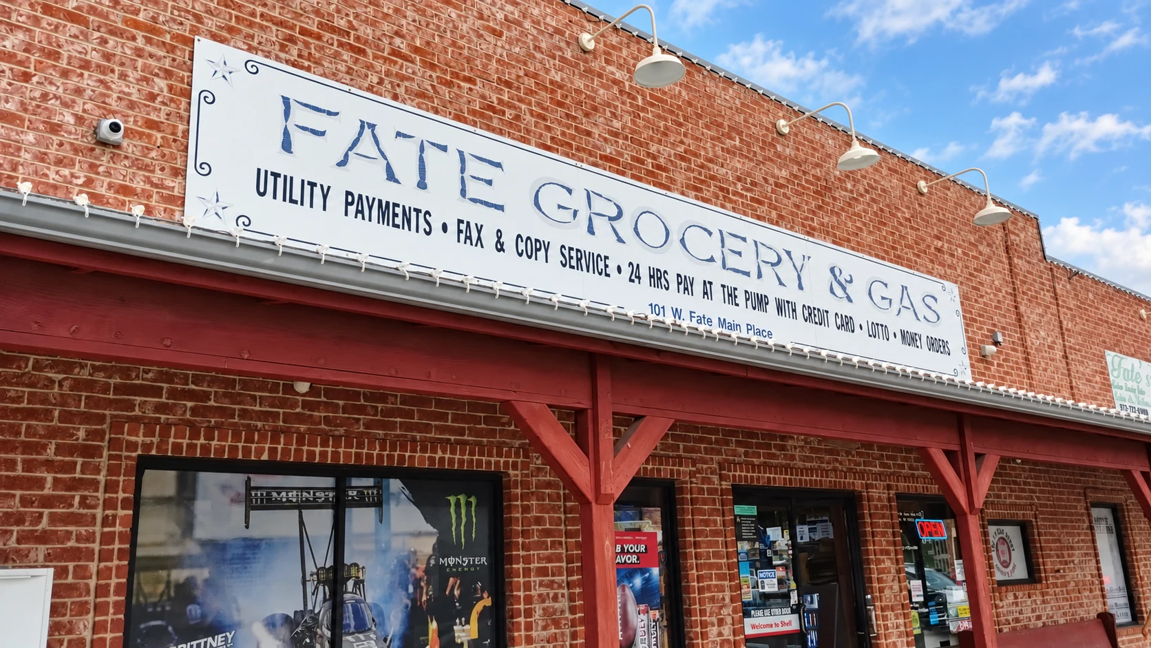 Fate Grocery & Gas sign and upper brick facade beneath a blue Texas sky.